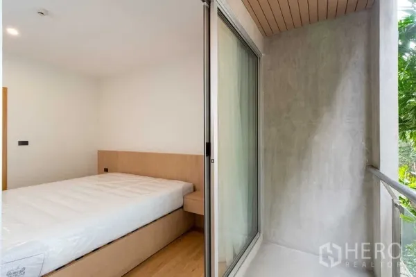Condominium for rent in Phra Khanong, Bangkok - Bedroom with sliding glass door opening to a compact balcony facing greenery.