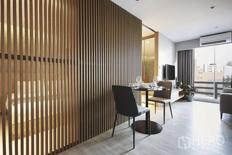 Apartment for rent in Khlong Toei, Bangkok - Compact dining nook beside a slatted wood partition leading to a bright living room with balcony.