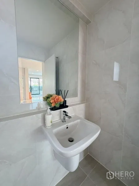 Detached House for rent or sale in Bang Phli, Samut Prakan - Compact powder room with wall-mounted sink, large mirror and light gray tiles.