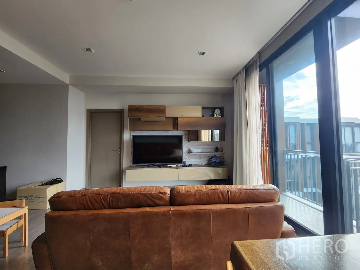 Condominium for rent in Watthana, Bangkok - Living room facing a floating TV console and balcony, filled with natural light.