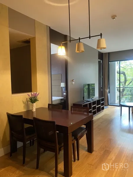 Condominium for rent in Watthana, Bangkok - Open-plan dining and living area with pendant lights, wood flooring, and a balcony facing greenery.
