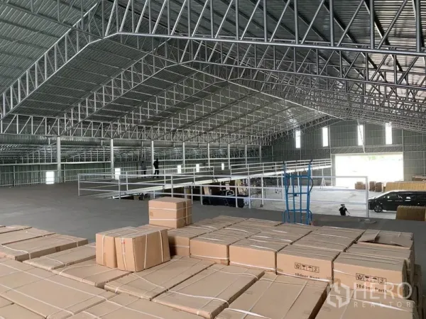 Warehouse for sale in Phra Nakhon Si Ayutthaya - High-clearance warehouse interior with steel truss roof and mezzanine, stacked with boxed inventory.