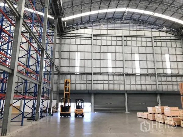 Warehouse for rent in Bang Pakong, Chachoengsao - Spacious loading area with multiple roller shutter doors, high ceiling, forklifts and smooth concrete flooring.