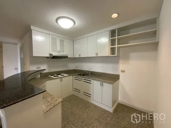 Condominium for rent or sale in Watthana, Bangkok - Compact U-shaped kitchen featuring white cabinets, granite countertops, and electric cooktop.