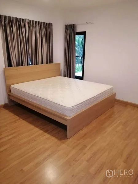 Townhouse for rent in Wang Thonglang, Bangkok - Cozy bedroom with wooden bed frame, curtains and window view.