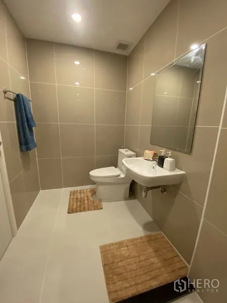 Townhouse for rent in Bang Kapi, Bangkok - Contemporary bathroom with beige tiles, toilet, sink, and mirror.