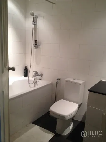 Condominium for rent in Pathum Wan, Bangkok - White-tiled bathroom with bathtub, handheld shower and toilet.