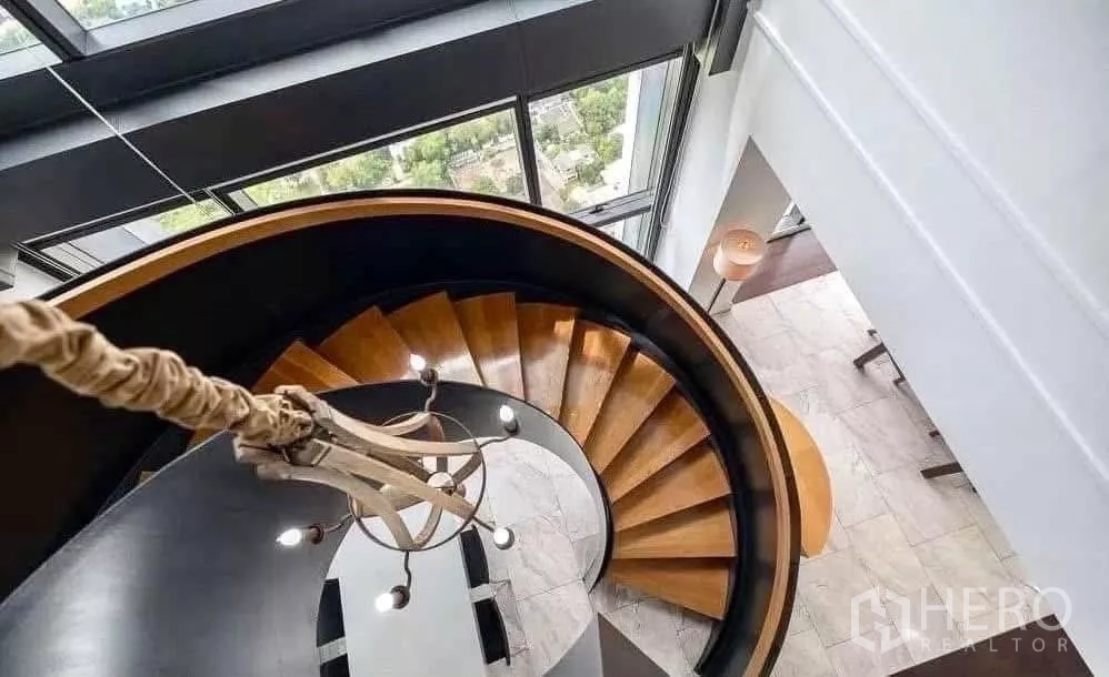 Condominium for rent in Sathon, Bangkok - Top-down view of curved wooden spiral staircase beside tall windows.