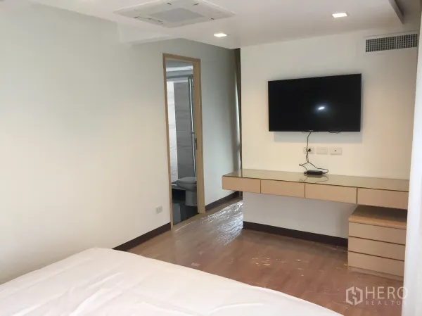 Condominium for rent in Pathum Wan, Bangkok - Primary bedroom with wall-mounted TV, floating desk and doorway to the ensuite bathroom.