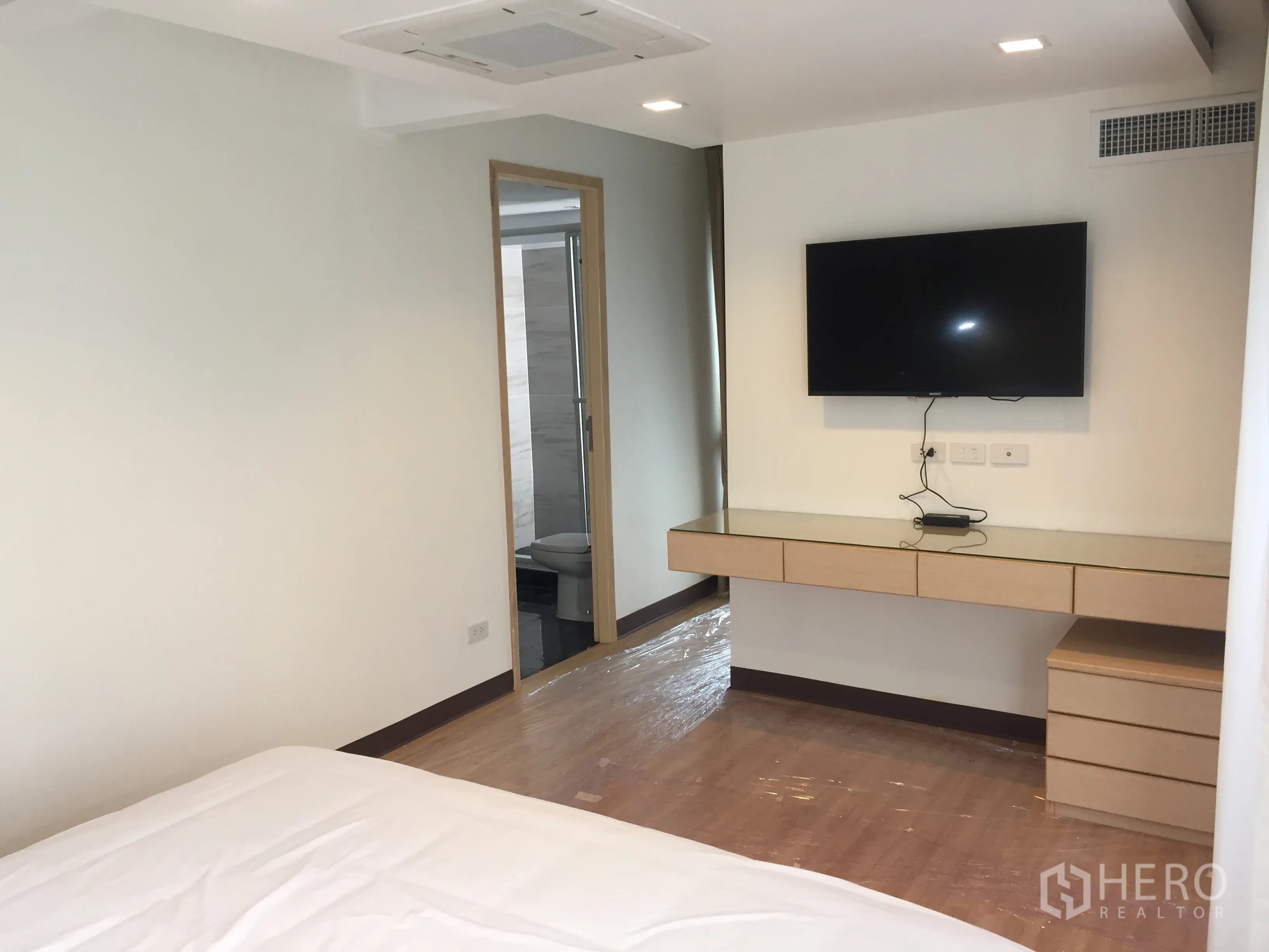 Condominium for rent in Pathum Wan, Bangkok - Primary bedroom with wall-mounted TV, floating desk and doorway to the ensuite bathroom.