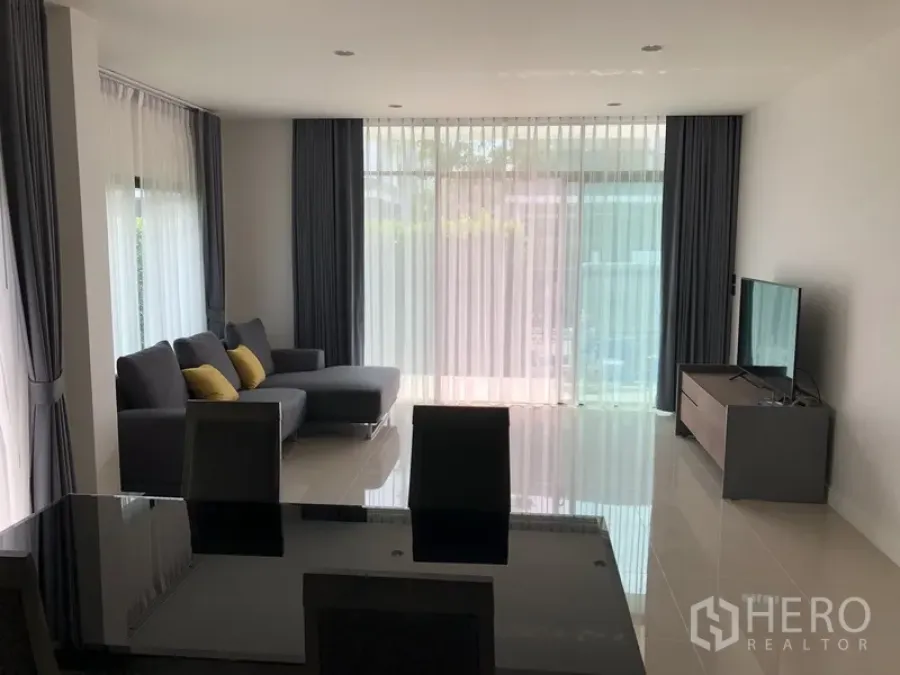Detached House for rent in Bang Kapi, Bangkok - Sunlit living room with L-shaped sofa, floor-to-ceiling sheer curtains, and a TV console.