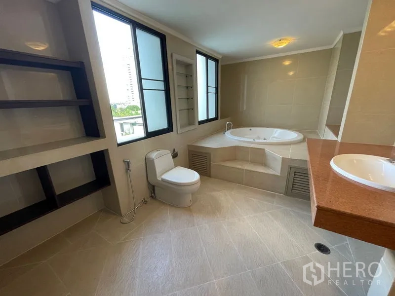 Condominium for rent in Watthana, Bangkok - Master bathroom featuring a corner jacuzzi tub, large windows and a long vanity counter.