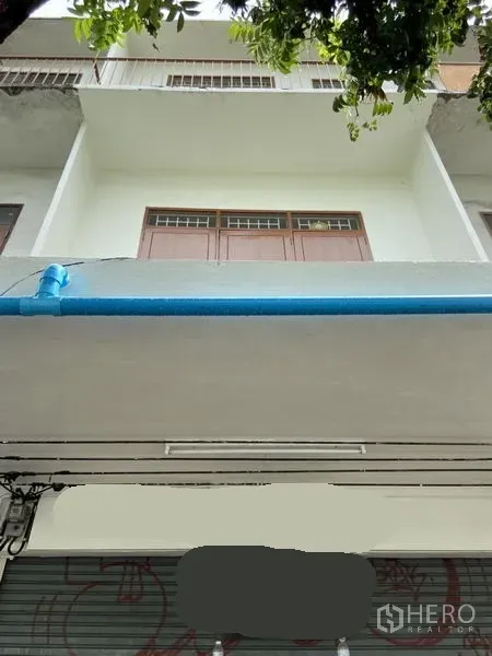 อาคารพาณิชย์ ให้เช่าในKhlong Toei, Bangkok - ภาพด้านหน้าตึกแถวติดถนน มีระเบียงชั้นบนและประตูม้วน ใต้ร่มไม้