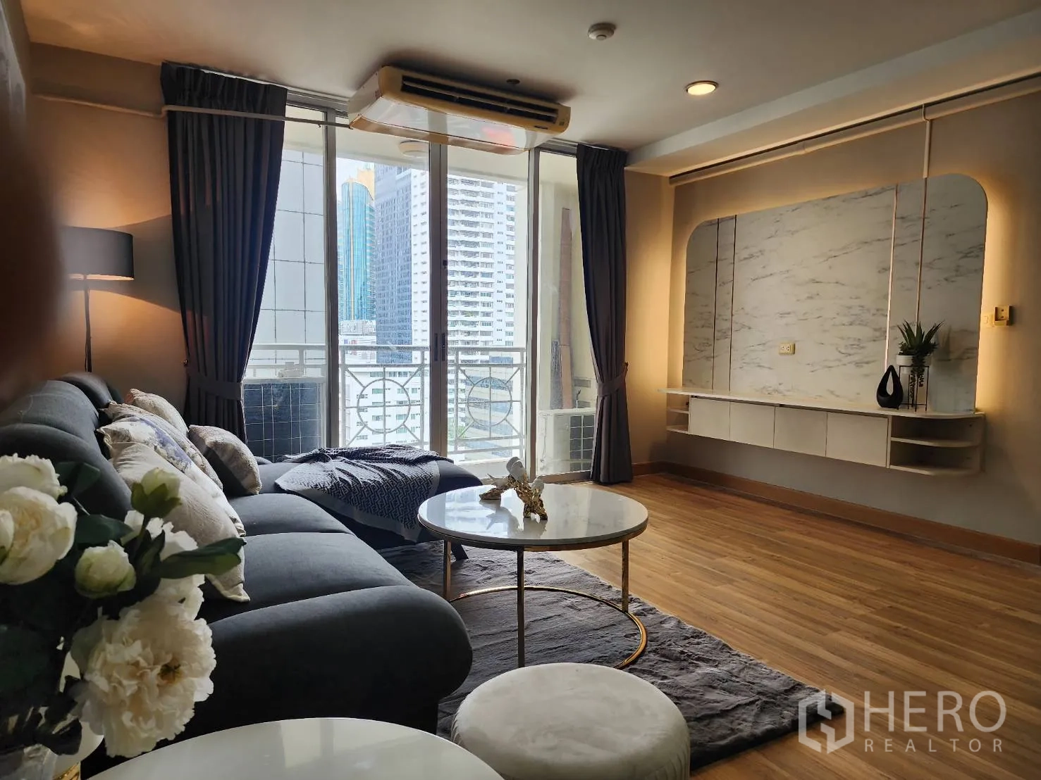 Condominium for rent in Watthana, Bangkok - Living area facing sliding glass doors to a balcony and a backlit TV wall.
