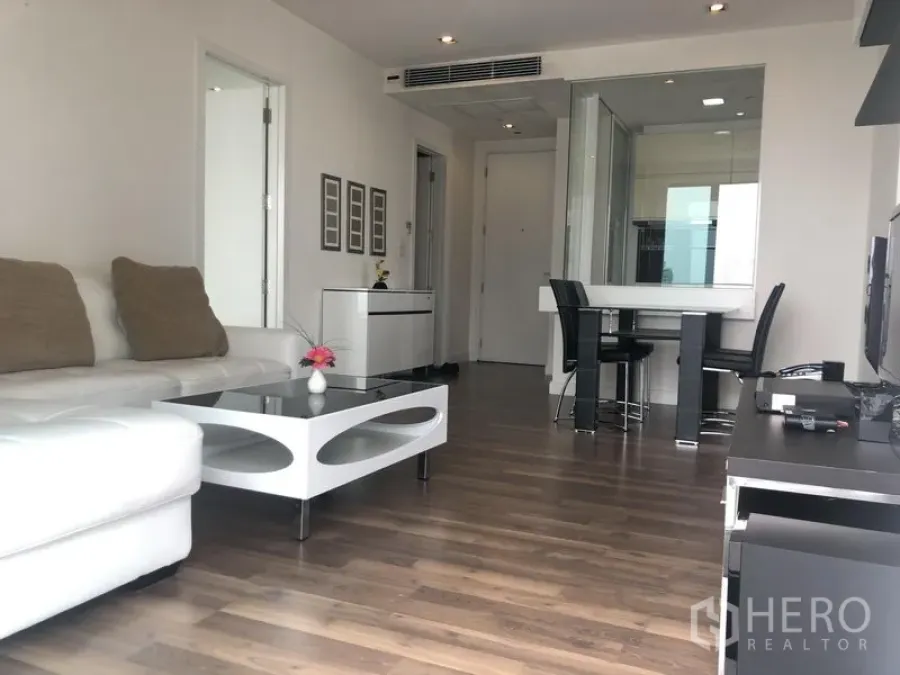Condominium for rent or sale in Phra Khanong, Bangkok - Bright living room with white L-shaped sofa, modern coffee table, wood floors, and a dining area in a Bangkok condo.