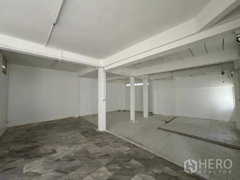 Home Office for rent in Watthana, Bangkok - Large ground-floor open space with columns and mixed tile flooring for workspace or parking.