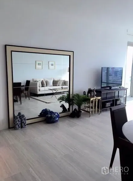 公寓 出租在Pathum Wan, Bangkok - 客厅一角设超大边框镜、电视柜与绿植，浅色木地板。