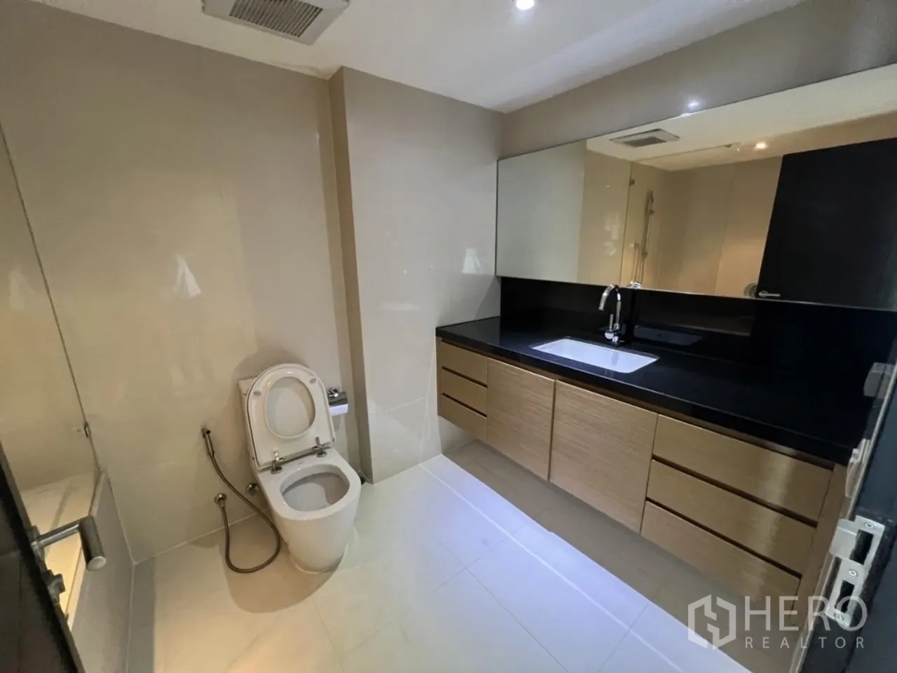 公寓 出租在Watthana, Bangkok - 宽敞浴室，长条黑色台面、超大镜子与坐便器。