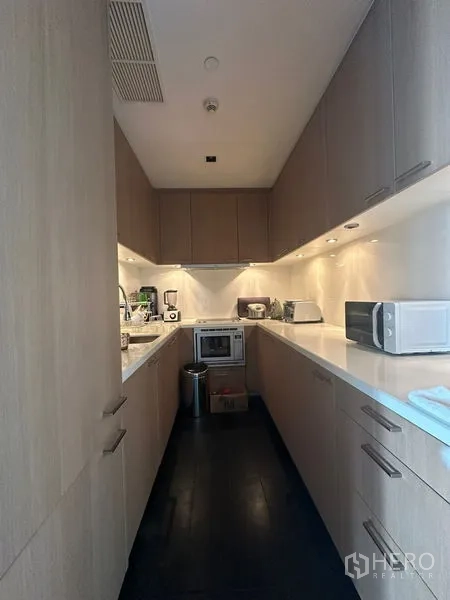 Condominium for rent or sale in Sathon, Bangkok - Galley kitchen with light wood cabinetry, white countertops, and built-in appliances.