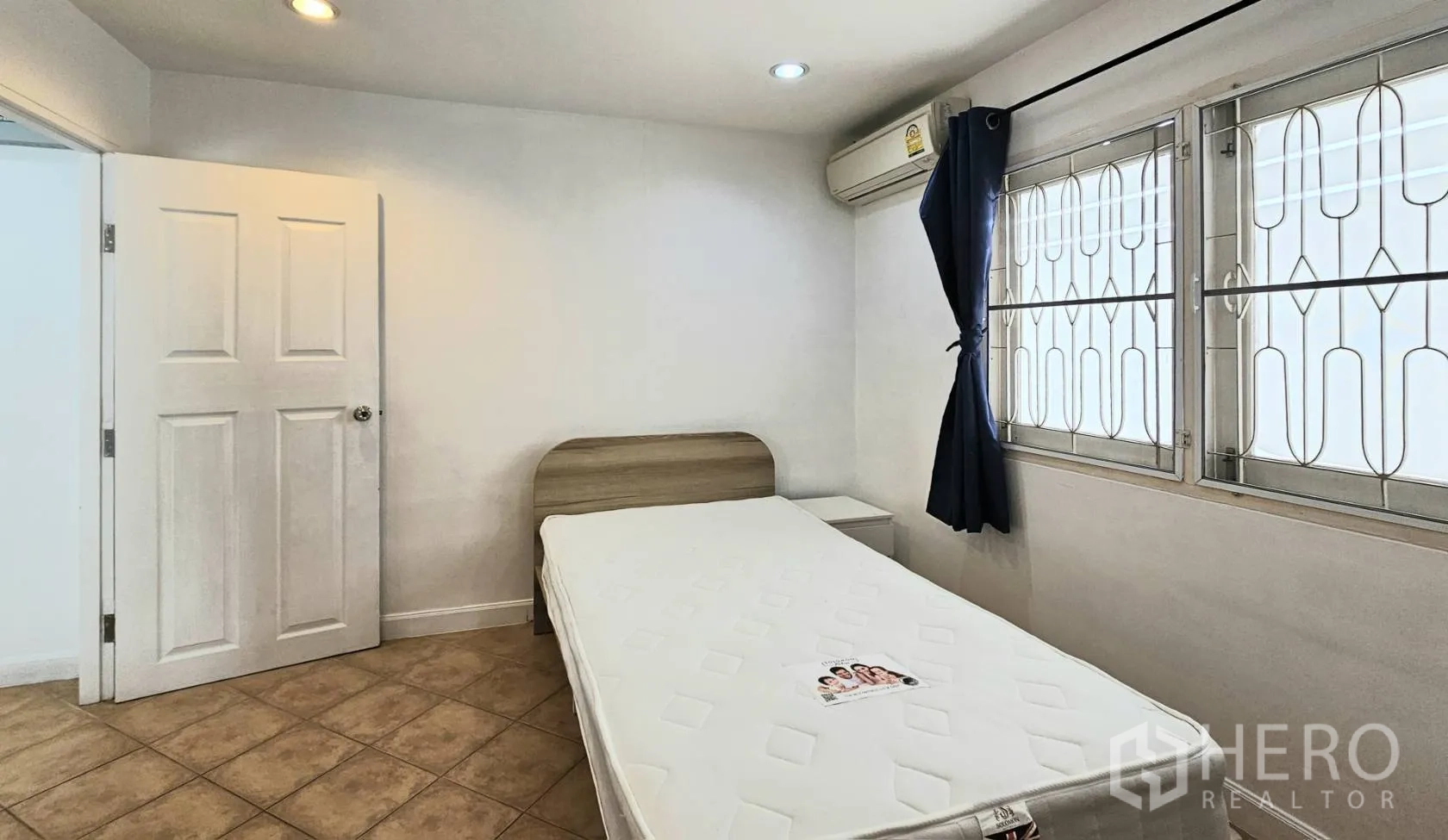 Detached House for rent in Saphan Sung, Bangkok - Compact bedroom with single bed, air conditioner, and barred windows with curtains.