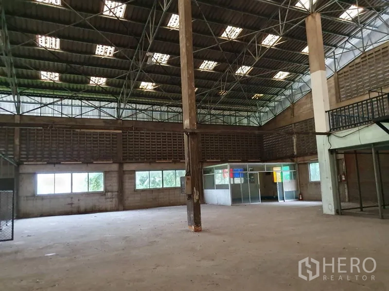 Factory for rent in Samut Prakan - Open production area with concrete floor, steel columns and a corner office booth beneath a high-clearance roof.