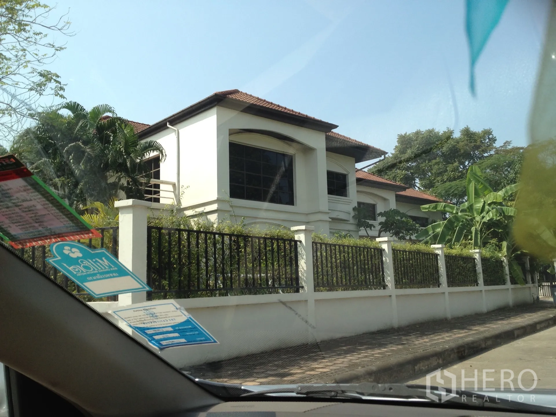 独立式住宅 出租在Nonthaburi - 两层白色独栋别墅，棕色瓦顶，大面积窗户与黑色金属围栏，绿树环绕，位于暖武里帕克烈。