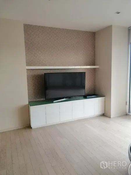 公寓 出租在Watthana, Bangkok - 内置电视墙，配平板电视、悬空置物架与白色地柜，浅色木地板。