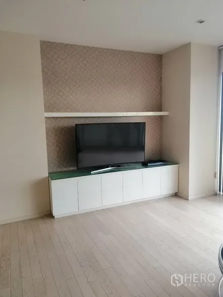 公寓 出租在Watthana, Bangkok - 内置电视墙，配平板电视、悬空置物架与白色地柜，浅色木地板。