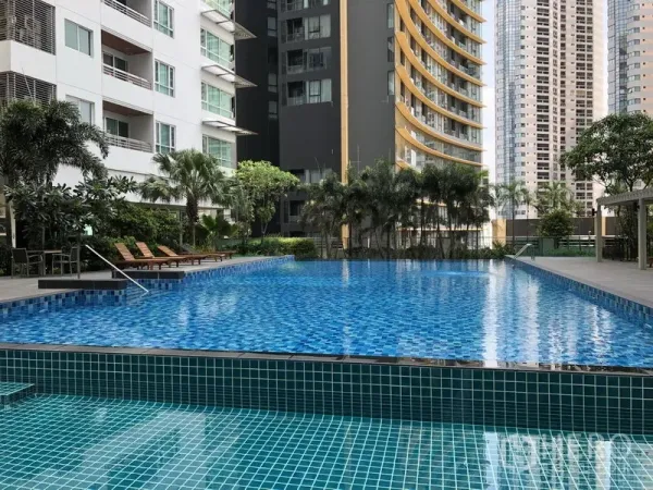 Apartment for rent in Khlong Toei, Bangkok - Resort-style outdoor swimming pool with blue tiles, sun loungers, palm trees and surrounding high-rise apartment buildings in Khlong Toei, Bangkok.