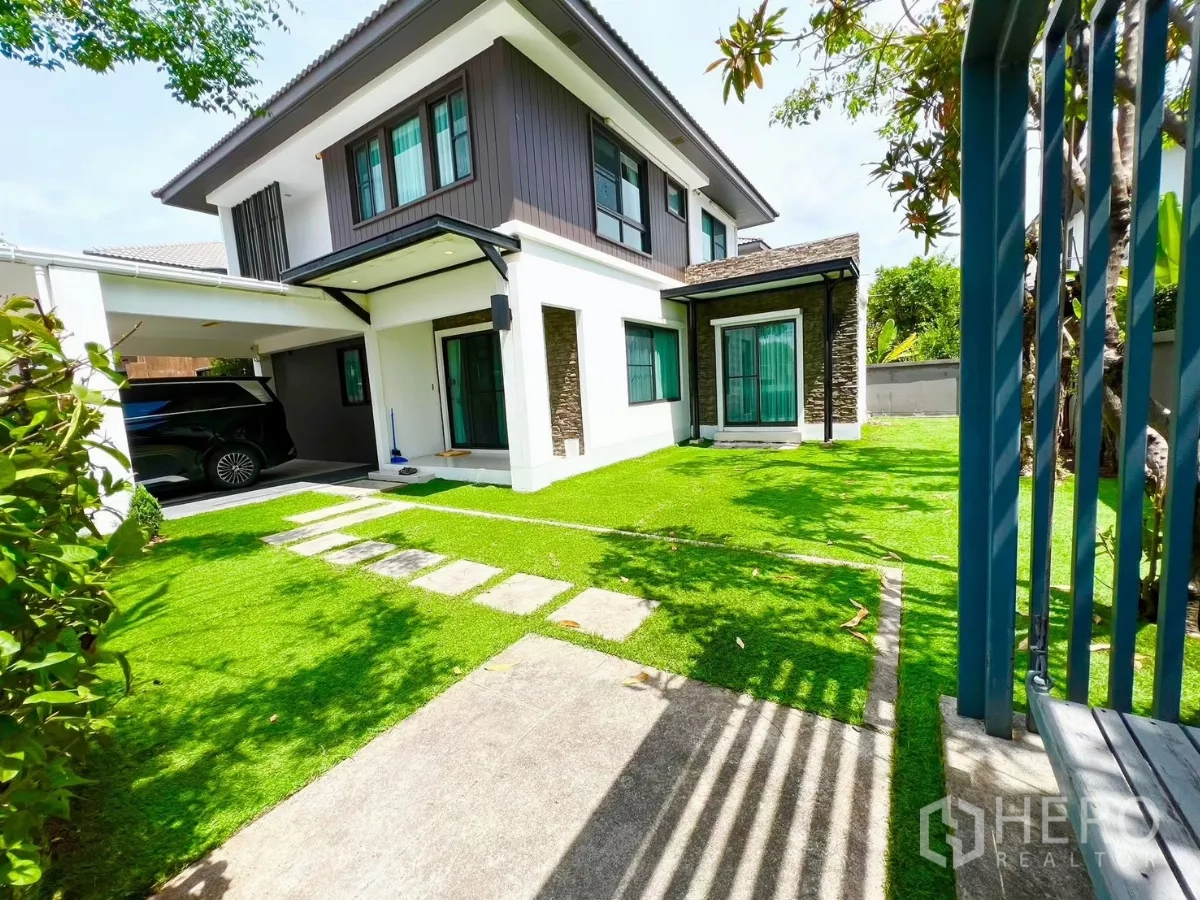 Detached House for rent or sale in Bang Phli, Samut Prakan - Sunny side yard with green lawn, stepping-stone path and covered parking beside the house.