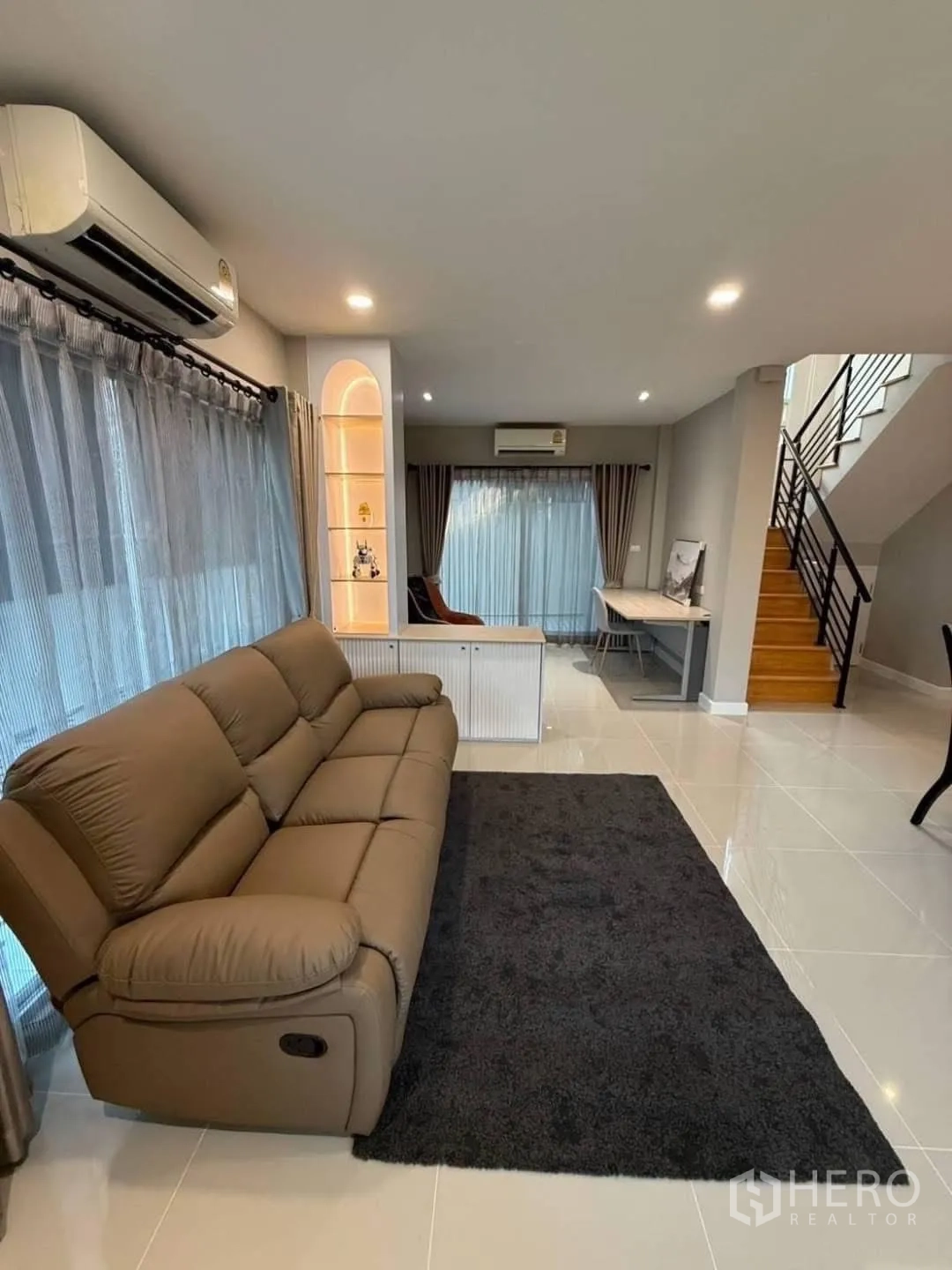 Detached House for rent in Prawet, Bangkok - Spacious living room with brown recliner sofa, dark rug and staircase.