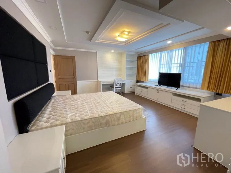 Condominium for rent in Watthana, Bangkok - Guest bedroom with built-in cabinetry, desk, TV console, and a big window with gold curtains.