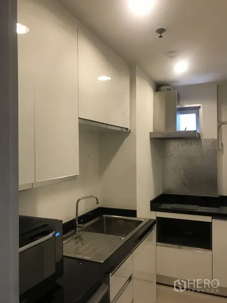 Condominium for rent or sale in Huai Khwang, Bangkok - Galley kitchen with glossy white cabinets, cooktop, range hood and a small window.