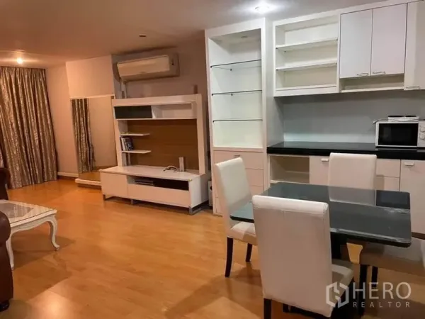 Condominium for rent or sale in Watthana, Bangkok - Dining corner beside built-in TV console, shelving, and long curtains on wood floors.