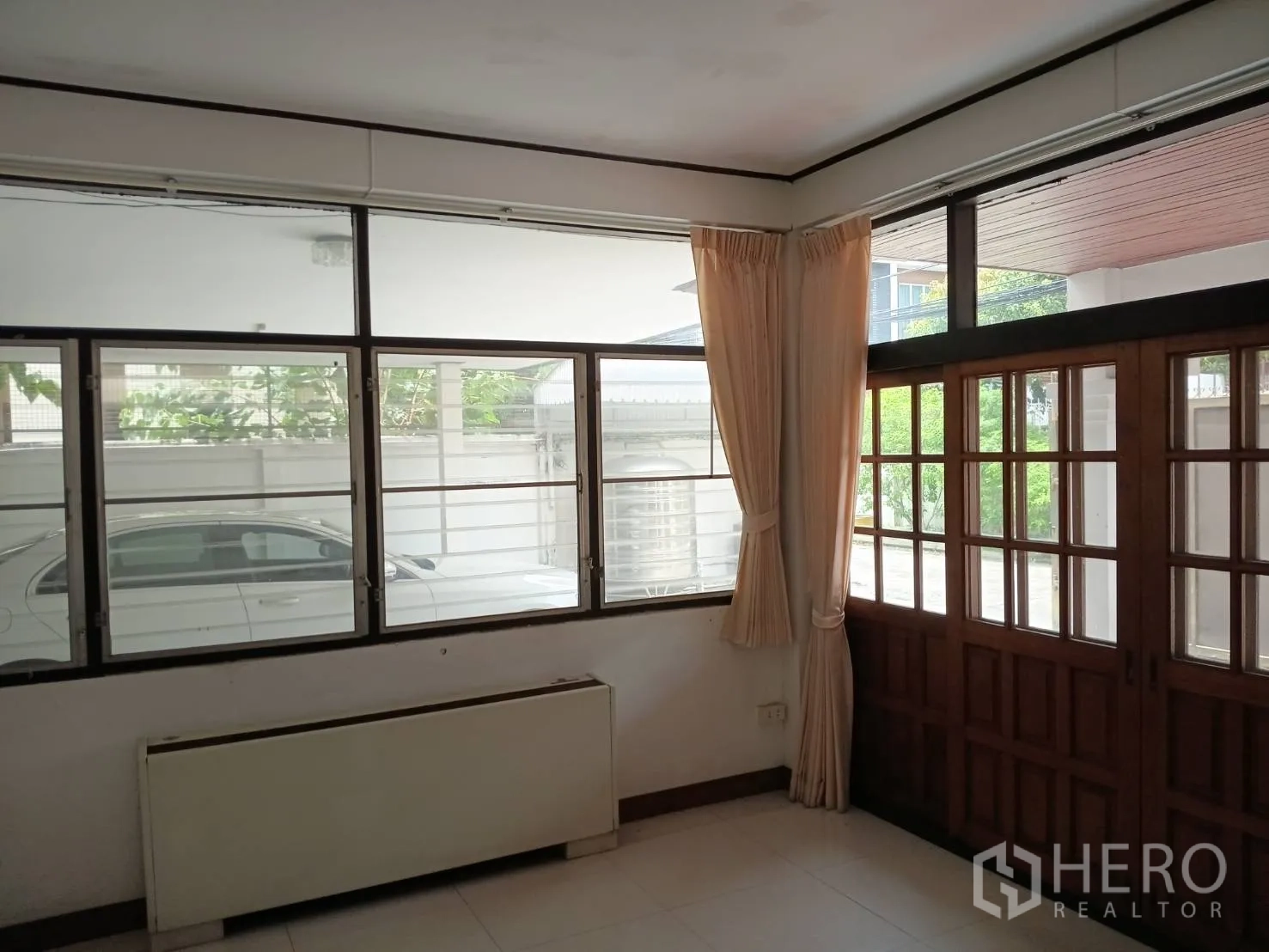 Detached House for sale in Watthana, Bangkok - Living area with large windows and wooden doors facing the driveway.