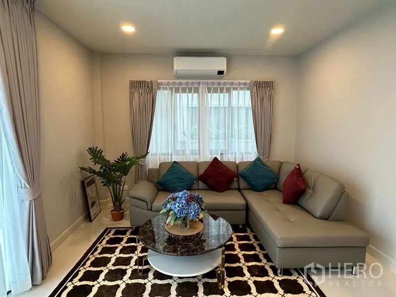Detached House for rent in Bang Phli, Samut Prakan - Cozy living room with L-shaped sofa, marble-top coffee table, patterned rug and large windows.