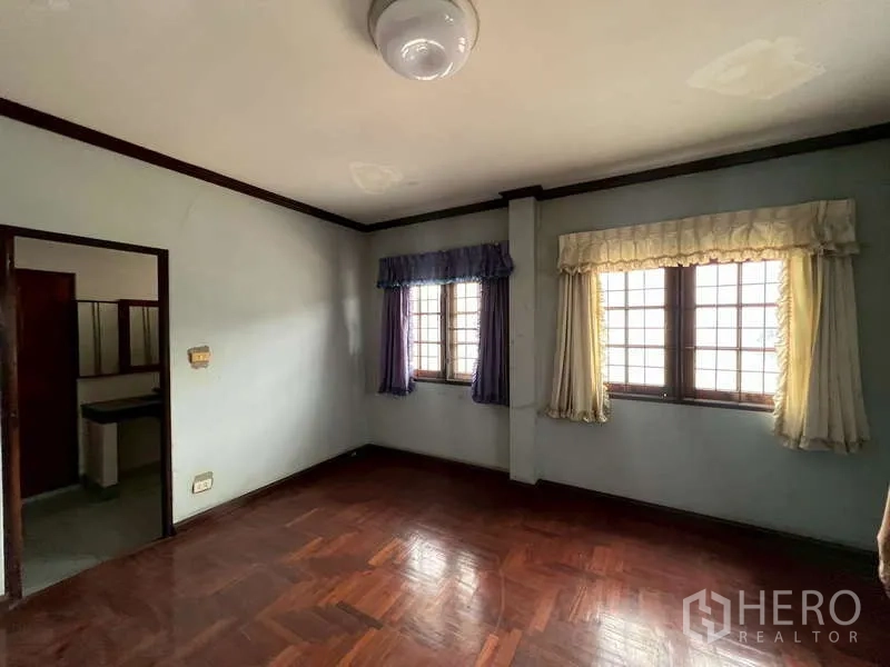 Detached House for rent in Prawet, Bangkok - Empty bedroom with parquet wood flooring, curtained windows and door to bathroom.