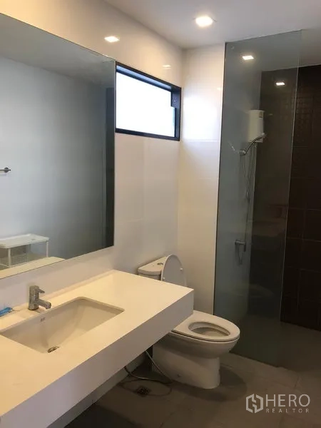 Townhouse for rent or sale in Saphan Sung, Bangkok - Modern bathroom with wide mirror, white vanity, toilet and glass-enclosed shower.