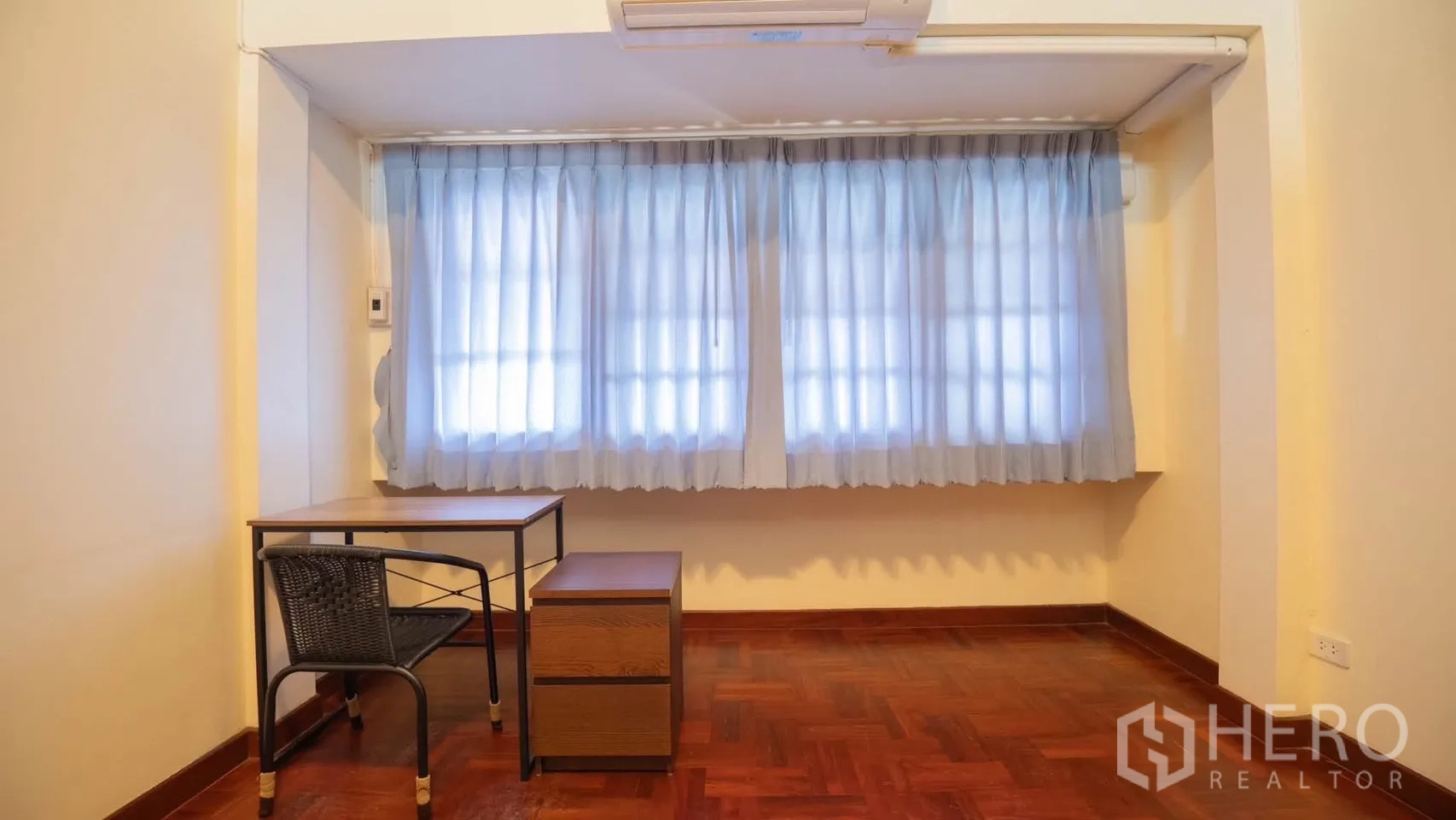 Townhouse for rent in Watthana, Bangkok - Bright study nook with desk, chair, air conditioner, and curtained windows over parquet flooring.