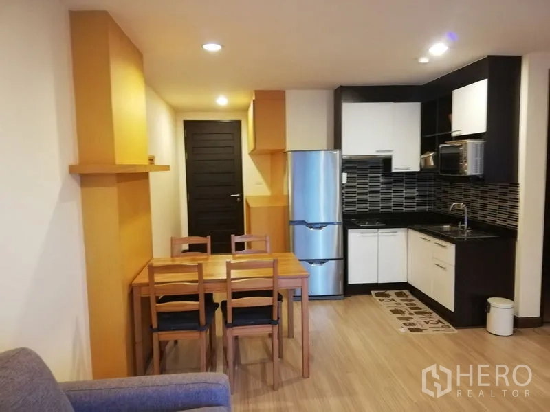 Condominium for rent in Watthana, Bangkok - Dining corner beside a modern kitchen with stainless refrigerator and ample cabinetry.