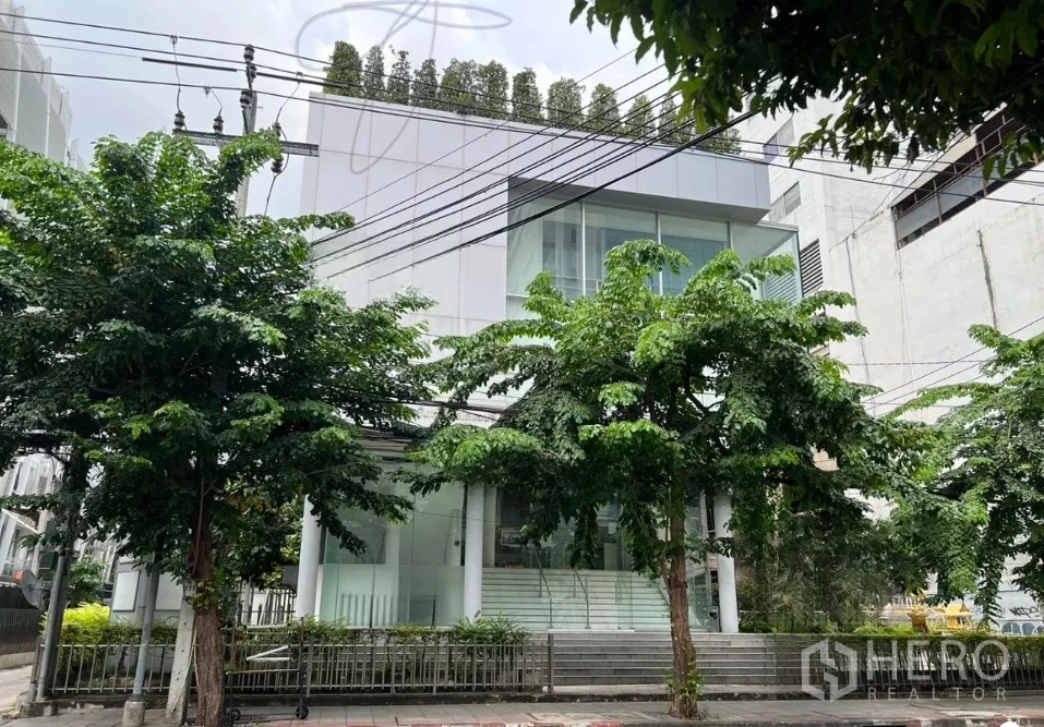 Office Space for rent in Bang Rak, Bangkok - Modern glass-front office building on a tree-lined street in Bangkok.