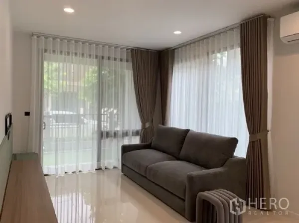 บ้าน ให้เช่าในBang Kapi, Bangkok - ห้องนั่งเล่นอบอุ่น โซฟาสีเทา มุมหน้าต่างกว้างและผ้าม่านทึบสูงจรดเพดาน