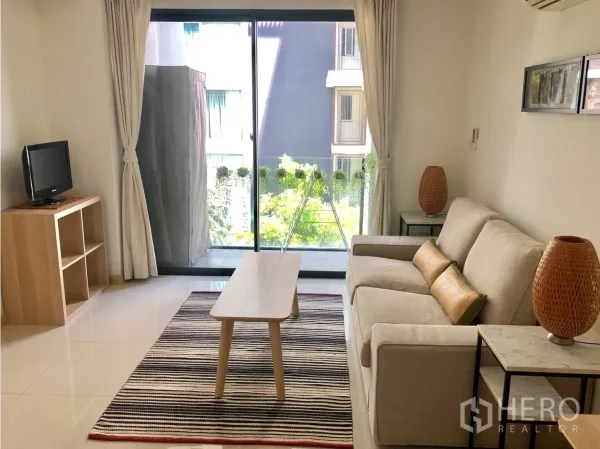 คอนโด ให้เช่าในWatthana, Bangkok - ห้องนั่งเล่นสว่างมีโซฟา พรม และประตูกระจกออกสู่ระเบียงเห็นต้นไม้