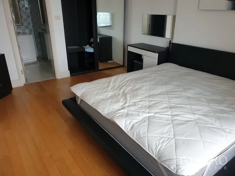 Condominium for rent or sale in Khlong Toei, Bangkok - Spacious bedroom with large bed, wooden flooring, mirrored wardrobe and doorway to the bathroom.