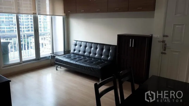 公寓 出租在Bang Rak, Bangkok - 客厅采光充足，黑色皮沙发，落地窗与城市景观，木地板。