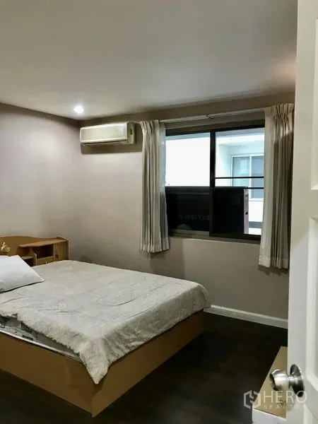 Condominium for rent in Watthana, Bangkok - Cozy bedroom with double bed, window with light curtains, and wall-mounted air conditioner.