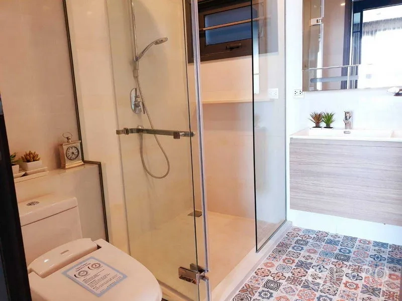 公寓 出租或出售在Khlong Toei, Bangkok - 明亮浴室，玻璃淋浴间、浴室柜、坐便器与花砖地面。