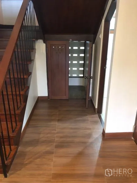 Detached House for rent in Watthana, Bangkok - Hallway beneath wooden staircase with storage and wood-look tile flooring.