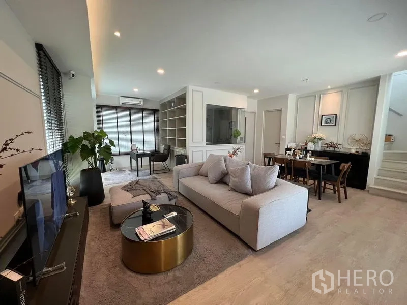 Detached House for rent or sale in Prawet, Bangkok - Open-plan living area with sofa, TV console and a work corner by large windows.