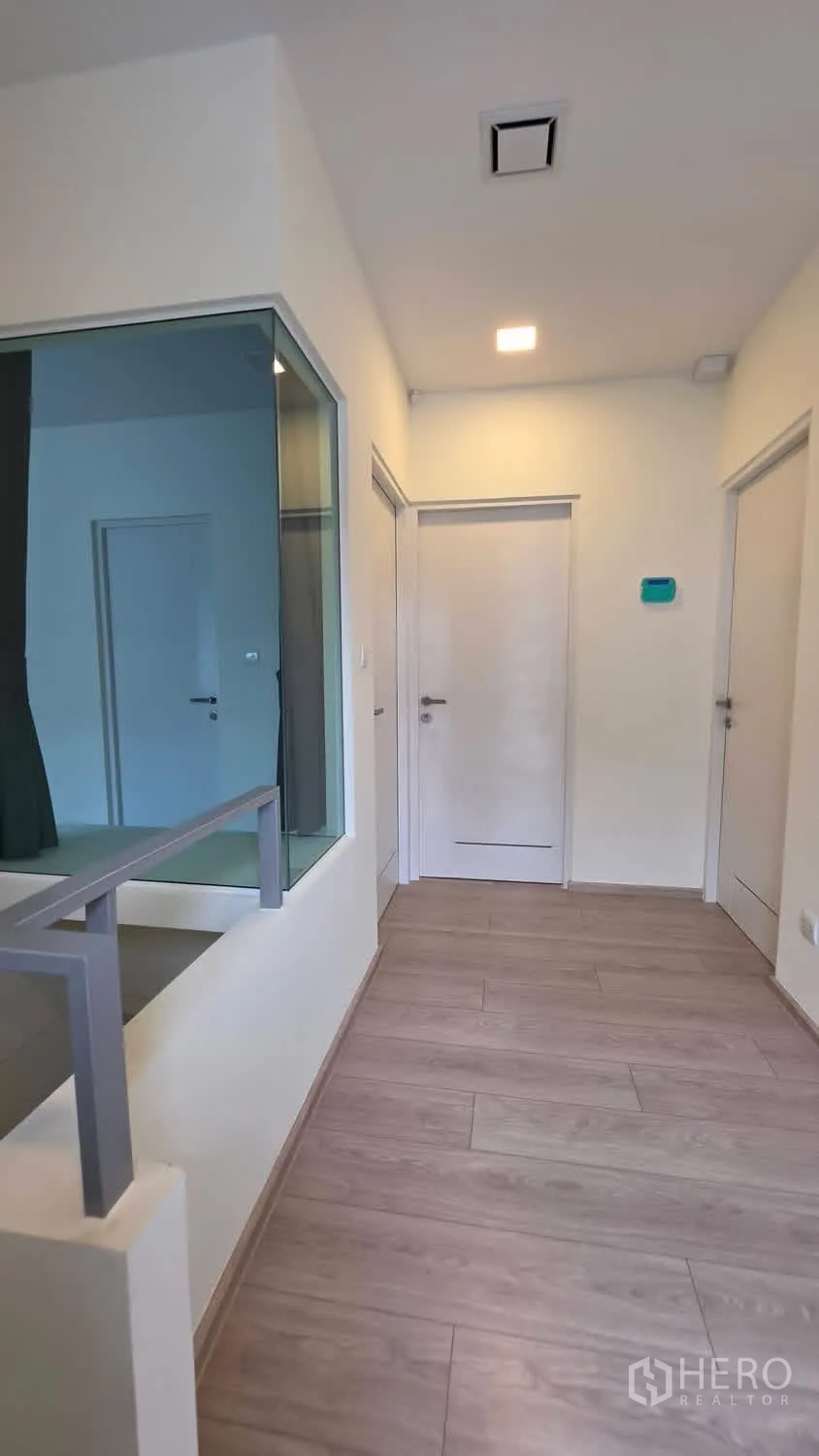Detached House for rent in Bang Phli, Samut Prakan - Upstairs hallway with glass partition, bedroom doors, and wood flooring.
